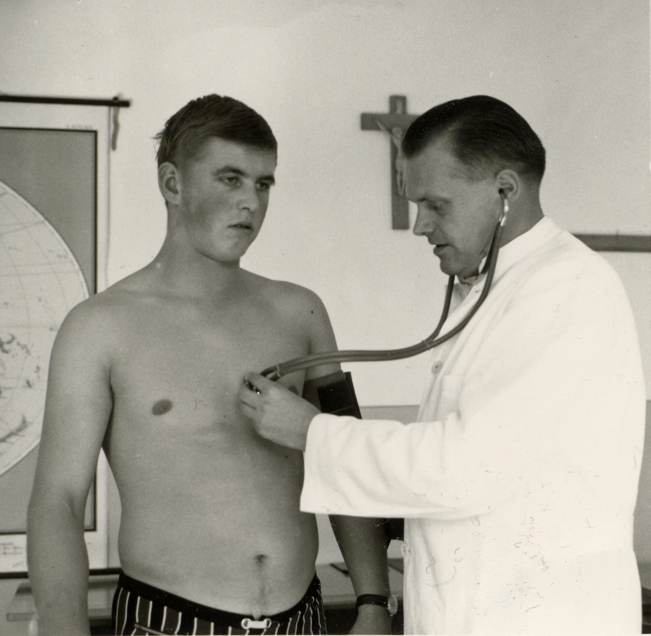 Schwarz-Weiß-Foto: Ein junger Mann mit freiem Oberkörper steht bei der Musterung 1968 vor einem Arzt.